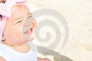 Cute Sweet 1 Year Old Baby Girl Toddler Sits on Beach Sand by Ocean Smiling. Sweet Face Expression. Bright Sunny Day. Parenting