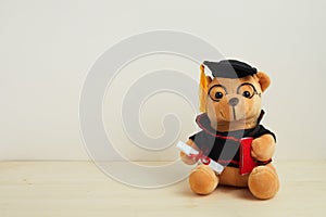 Cute teddy bear with nice graduation clothes and diploma on wooden table. School concept