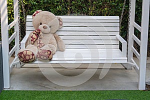 Cute teddy bear sitting on a white wooden swing in the garden and green natural background decoration