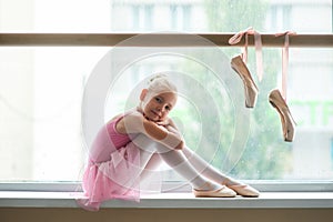 Cute teen ballerina sitting on windowsill.