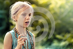 A cute teen girl with blonde hair chants a mantra on a rosary. Yoga, spirituality concept