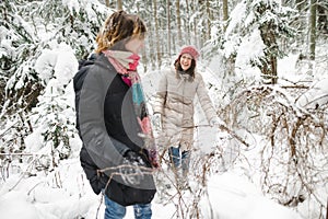 Cute teen girl and her mother having fun on a walk in snow covered pine forest on chilly winter day. Teenage child exploring