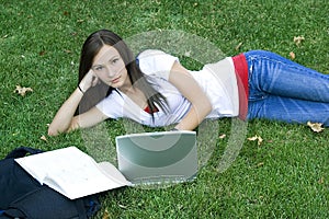 Cute teen girl laying down on the grass studying