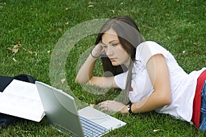 Cute teen girl laying down on the grass studying