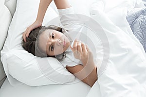 Cute teen girl lying in bed with termometer in her hand