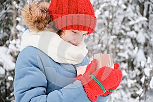 cute teen girl opens a gift box, christmas present, outdoor in winter, child in scarf, mittens and hat