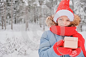 cute teen girl opens gift box, christmas present, outdoor in winter, child in scarf, mittens and santa hat