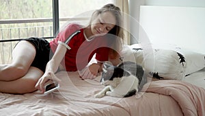 Cute teen girl with pink hair plays with cat on bed, then takes phone