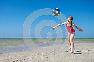 Cute teen girl playing and having fun with ball on beach at sunny summer day