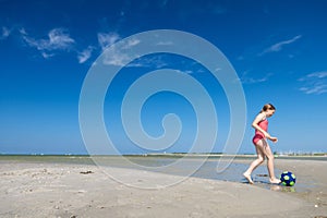 Cute teen girl playing and having fun with ball on beach at sunny summer day