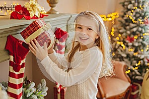 Cute teen girl with present near Christmas tree smiiling