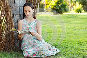 Cute teen girl reading book sitting on green grass