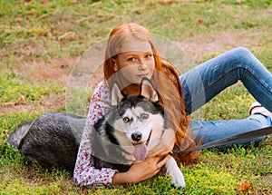 Cute teen girl with red long hair walks with her husky breed dog in the autumn park. Children and dogs.