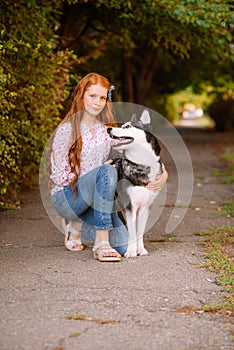 Cute teen girl with red long hair walks with her husky breed dog in the autumn park. Children and dogs.