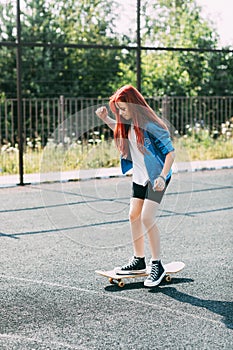 Cute teen girl rides a skateboard on a sports field