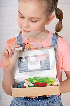 Cute teen girl with two pigtails holding a whole box of colorful marmalade