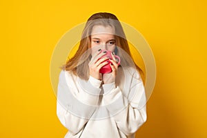 Cute teen girl wearing a white hoodie warms on a hot cup of tea.