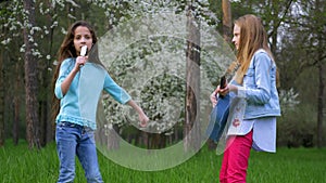 Cute teen girlfriends playing his guitar outdoors. little girls sing songs comb hair and dancing together