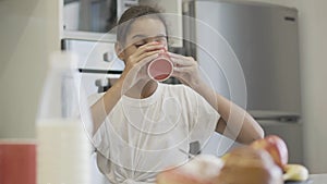 Cute teenage African American girl drinking tea or coffee in the morning at home. Portrait of pretty teenager having