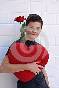 Cute teenage boy with a heart shaped pillow and red rose