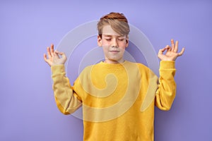 Cute teenage boy keep calm, meditating, isolated on purple studio background