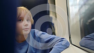 Cute teenage boy rides in a subway train carriage or by rail. Child is watching the rain from the window