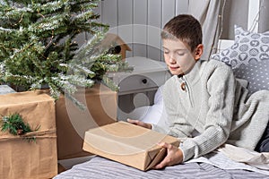 A cute teenage boy in a sweater pulls out gifts from under a Christmas tree. New Year& x27;s morning. Christmas Family