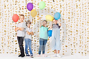 Cute teenage boys and girls is standing together in a room and holding colorful balloons