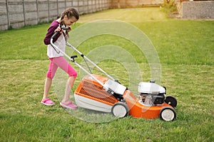 Cute teenage child girl working in garden, mowing green grass with lawn-mower on backyard on summer holiday. Concept of