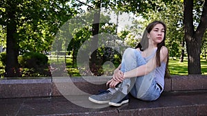 Cute teenage girl checking phone and waiting phone call sitting in park. Video footage HD shooting static camera.