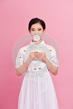 Cute teenage girl covering her mouth with lips lollipop, looking in camera and posing, standing against pink