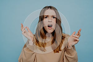 Cute teenage girl expressing disbelief and shock standing against blue studio wall