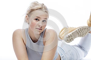 Cute teenage girl with freckles on her face. A blonde girl in a blue top, jeans and boots lies on the floor. Close-up. White