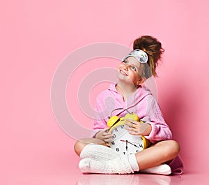 Cute teenage girl holding an alarm clock while sitting in a housecoat on the floor. photo