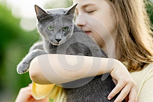 Cute teenage girl holding her pet cat on sunny summer day. Gorgeous grey Russian Blue breed cat outdoors