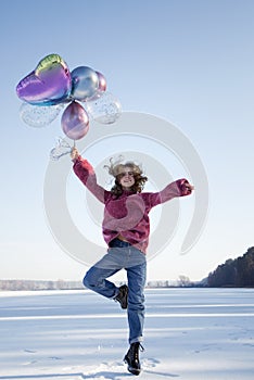Cute teenage girl, holding many colorful balloons in her hands, jumping up on the snowy ground