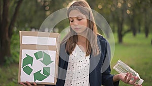 Cute teenage girl looking at box with recycle sign and plastic bottle smiling looking at camera. Portrait of pretty