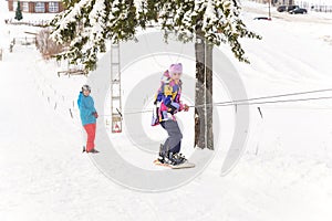 Cute teenage girl and mature male snowboarders using ski drag rope lift to rise up to the slope top at ski resor