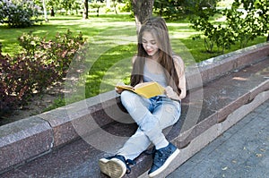 Cute teenage girl reading book sitting on the bench in park, studying outdoor.