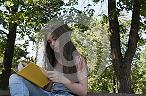 Cute teenage girl reading book sitting on the bench in park, studying outdoor.