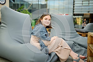 Cute teenage girl relaxing on a sitting pillow in outdoor cafe in Vilnius, Lithuania on warm and sunny summer day
