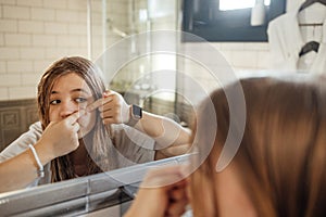 Cute teenage girl squeezes out a pimple on her cheek in the bathroom