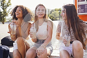 Cute teenage girls in casual summer clothes drinking tasty iced lemonade outdoors in the park