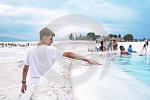 Cute teenager aged 15-18 reached out his hand and touched the water in the travertine pool in Pamukkale.