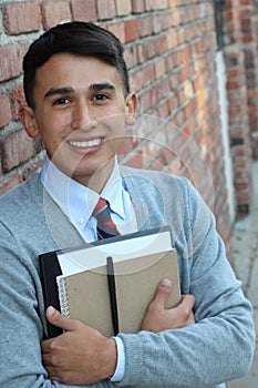 Cute teenager boy in formal high school uniform holding notebooks smiling