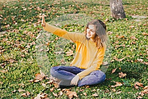 Cute teenager girl greeting friends outdoors by waving hand. Fall mood