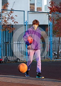 Cute teenager in violet hoodie playing basketball. Young boy with ball learning dribble and shooting on the city court. Hobby