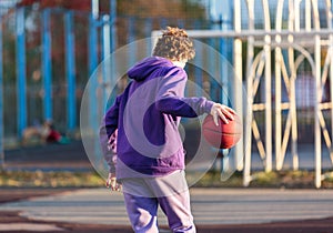 Cute teenager in violet hoodie playing basketball. Young boy with ball learning dribble and shooting on the city court. Hobby