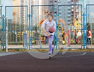 Cute teenager in a white t-shirt playing basketball outside. Young boy with ball learning dribble and shooting on the city court