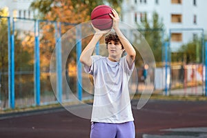 Cute teenager in a white t-shirt playing basketball outside. Young boy with ball learning dribble and shooting on the city court